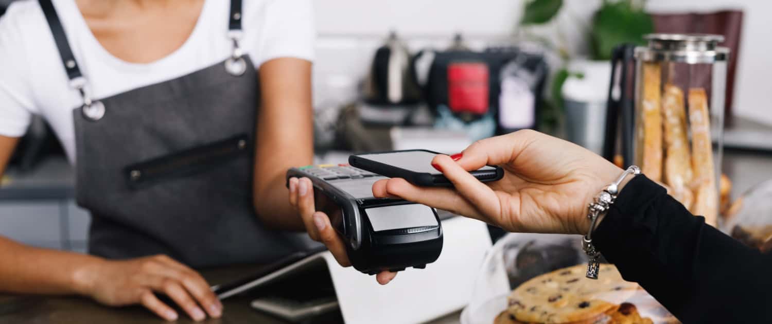 Customer making a contactless payment using a smartphone at a café counter.