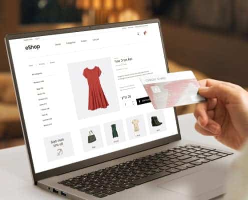 Person holding a credit card while shopping for clothes on a laptop.