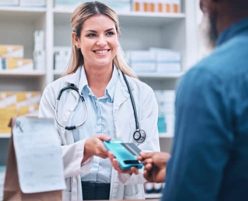 Smiling pharmacist accepting a contactless payment from a customer at a pharmacy counter.