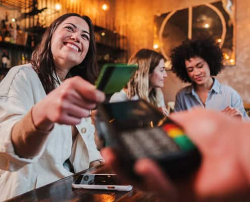 Smiling woman making a contactless payment with a credit card at a restaurant.